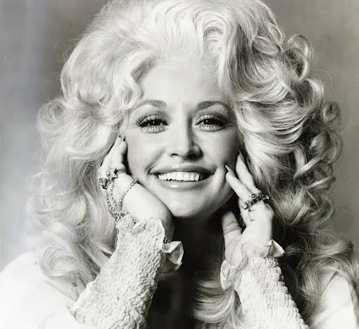 Black-and-white portrait of a smiling Dolly Parton, her hands framing her face